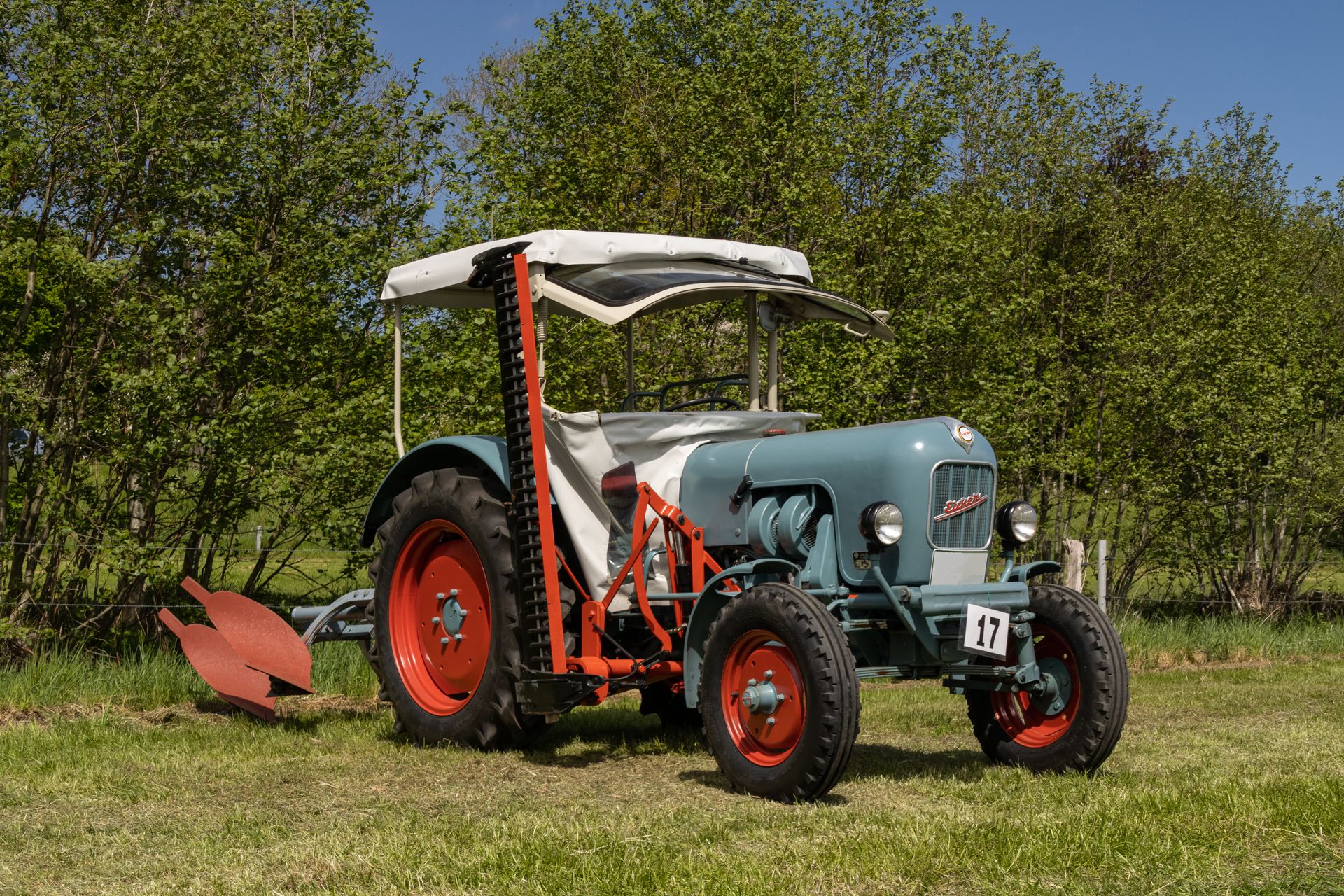 A classic tractor parked on a grassy field surrounded by trees, showcasing rural mechanical charm.