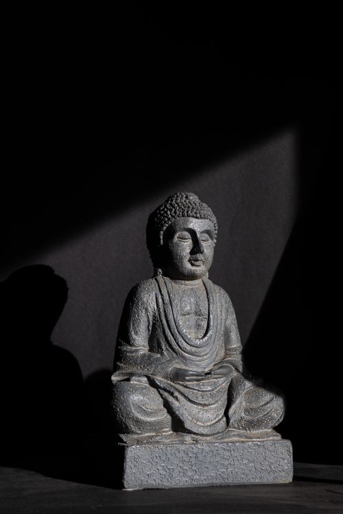 Free Elegant stone Buddha statue in meditative posture, captured in a dark, moody setting. Stock Photo