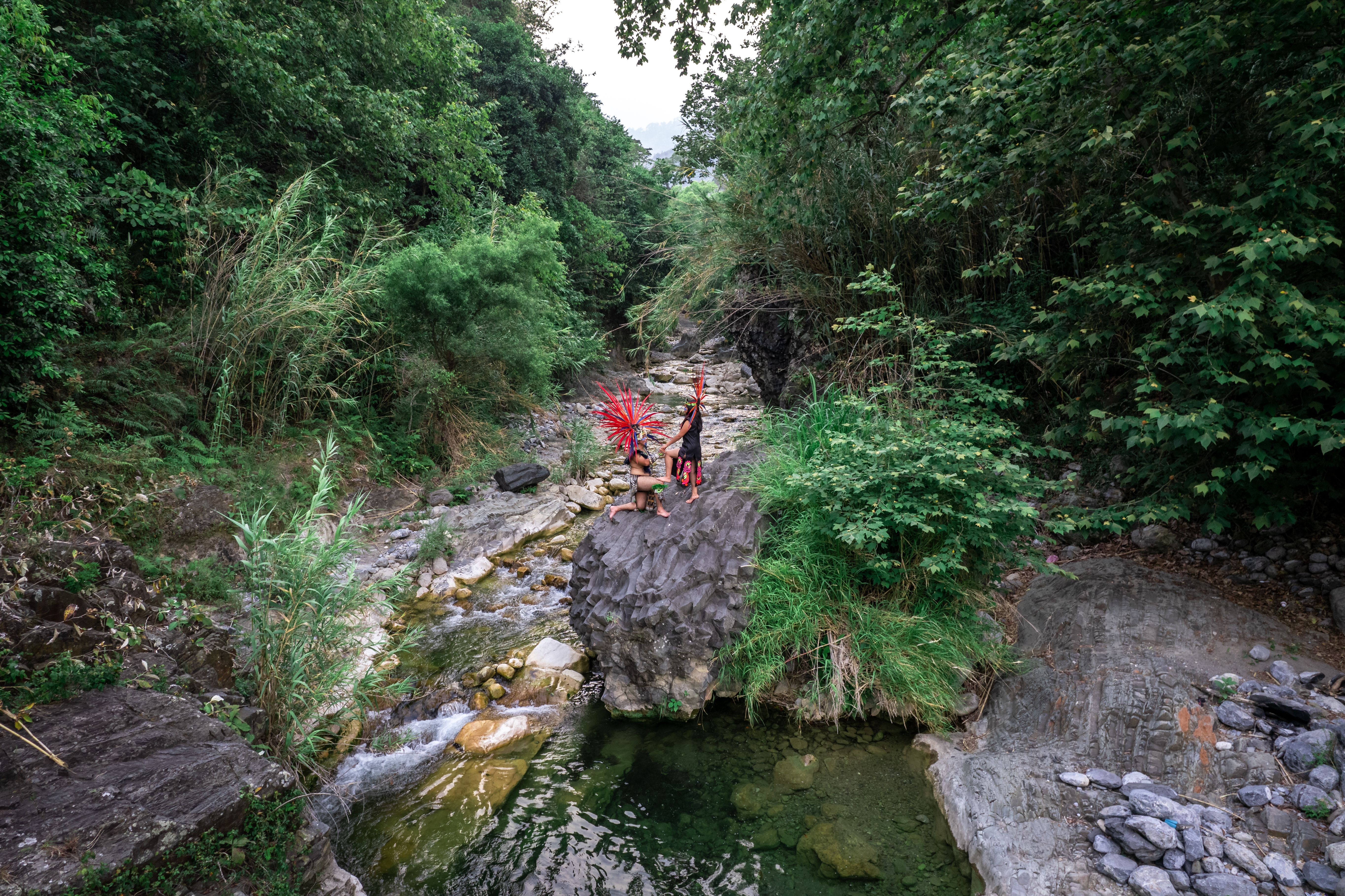 A couple in traditional attire stands by a scenic forest stream in Tlamanca de Hernández, Mexico.