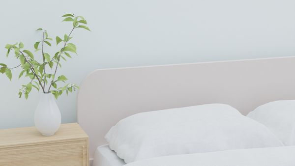Bedside table with a leafy sprig in a white vase beside a made bed — photo by dada _design on Pexels