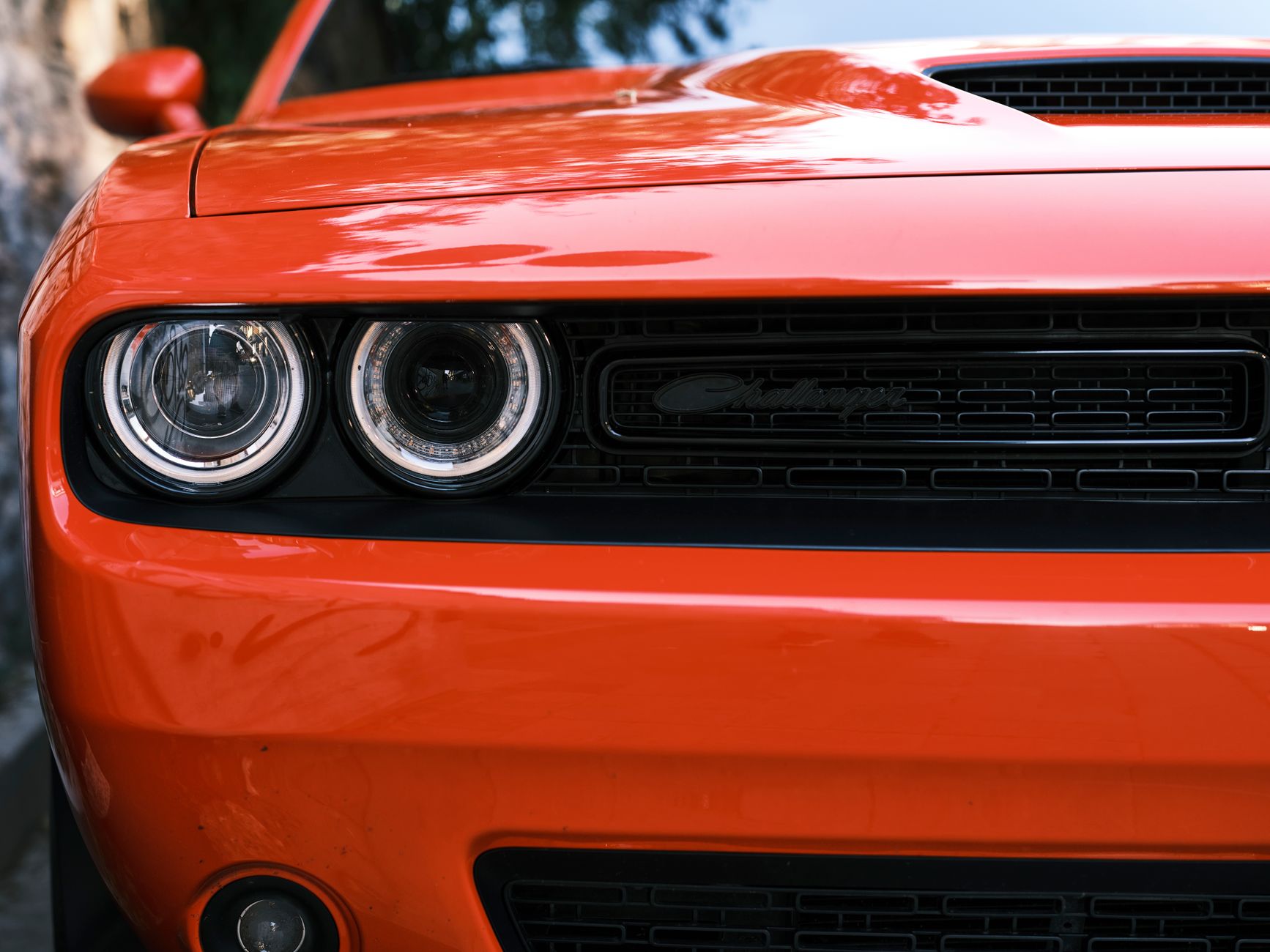 A detailed and vibrant close-up of a red Dodge Challenger's front grille and headlights, showcasing automotive design.