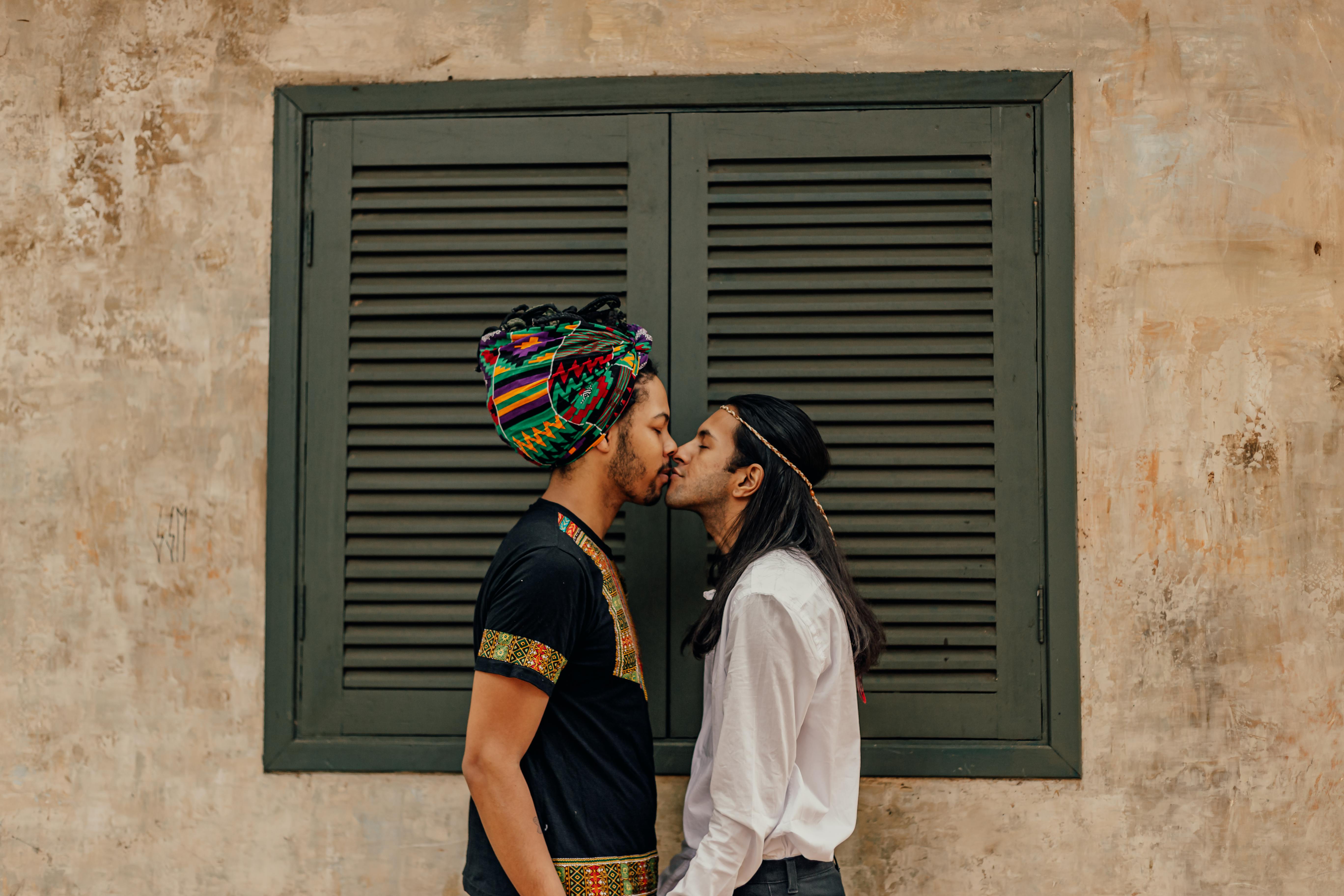 shot of two man kissing in front of window with closed shutters