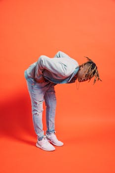 Stylish individual posing in denim outfit against vibrant orange background.