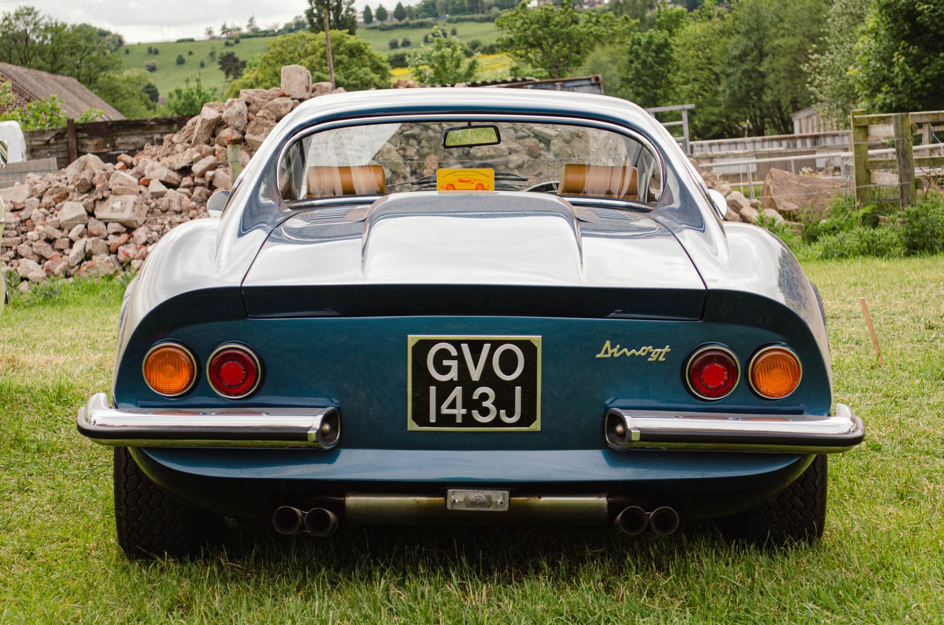 Rear view of a classic Ferrari Dino GT parked in a lush green field, exuding vintage charm.