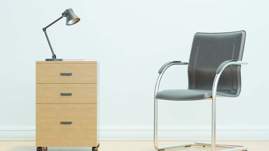 A minimalist office setup showcasing a sleek chair and wooden drawer unit with a desk lamp.