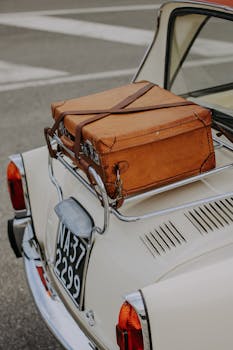 Close-up of a leather suitcase on a vintage car's luggage rack, showcasing travel style.
