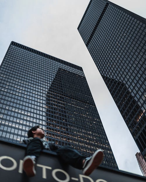 Low Angle Shot of a Man Sitting on a Roof with Skyscrapers in Background