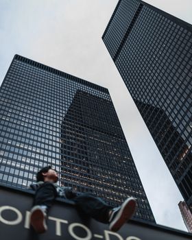 Low angle view of skyscrapers and person sitting in Toronto's urban skyline.