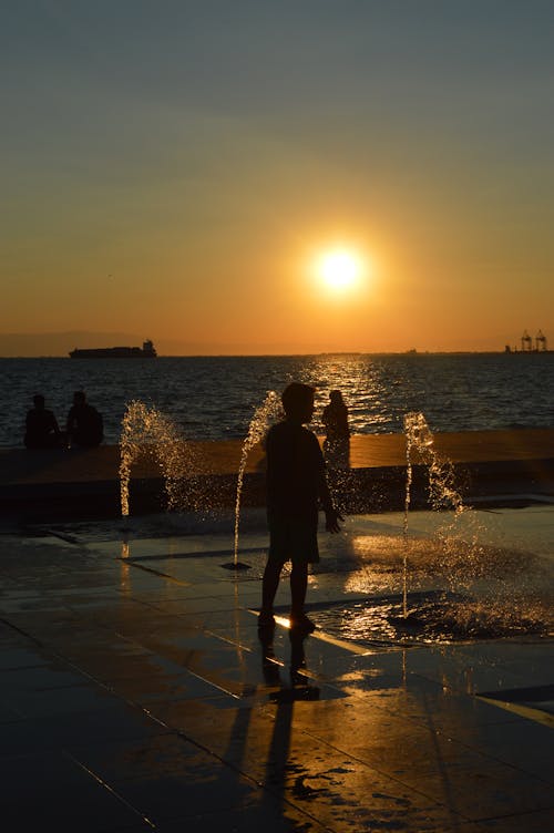 Free Silhouette of a Person Standing on a Water Fountain Stock Photo