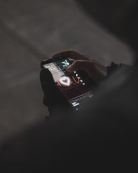 Close-up of a hand holding a smartphone displaying a heart icon, captured outdoors.