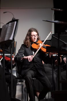 Violinist focused during a live orchestral performance, dressed in formal attire.