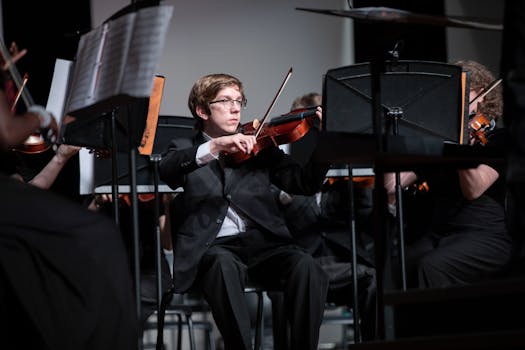 A violinist in a suit performs in an orchestral concert setting.