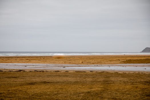Wide view of a tranquil sandy beach under an overcast sky with gentle waves, ideal for relaxation.