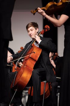 Young musician playing cello in an orchestral performance indoors.