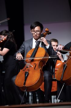 A focused musician plays the cello on stage during an orchestral performance.