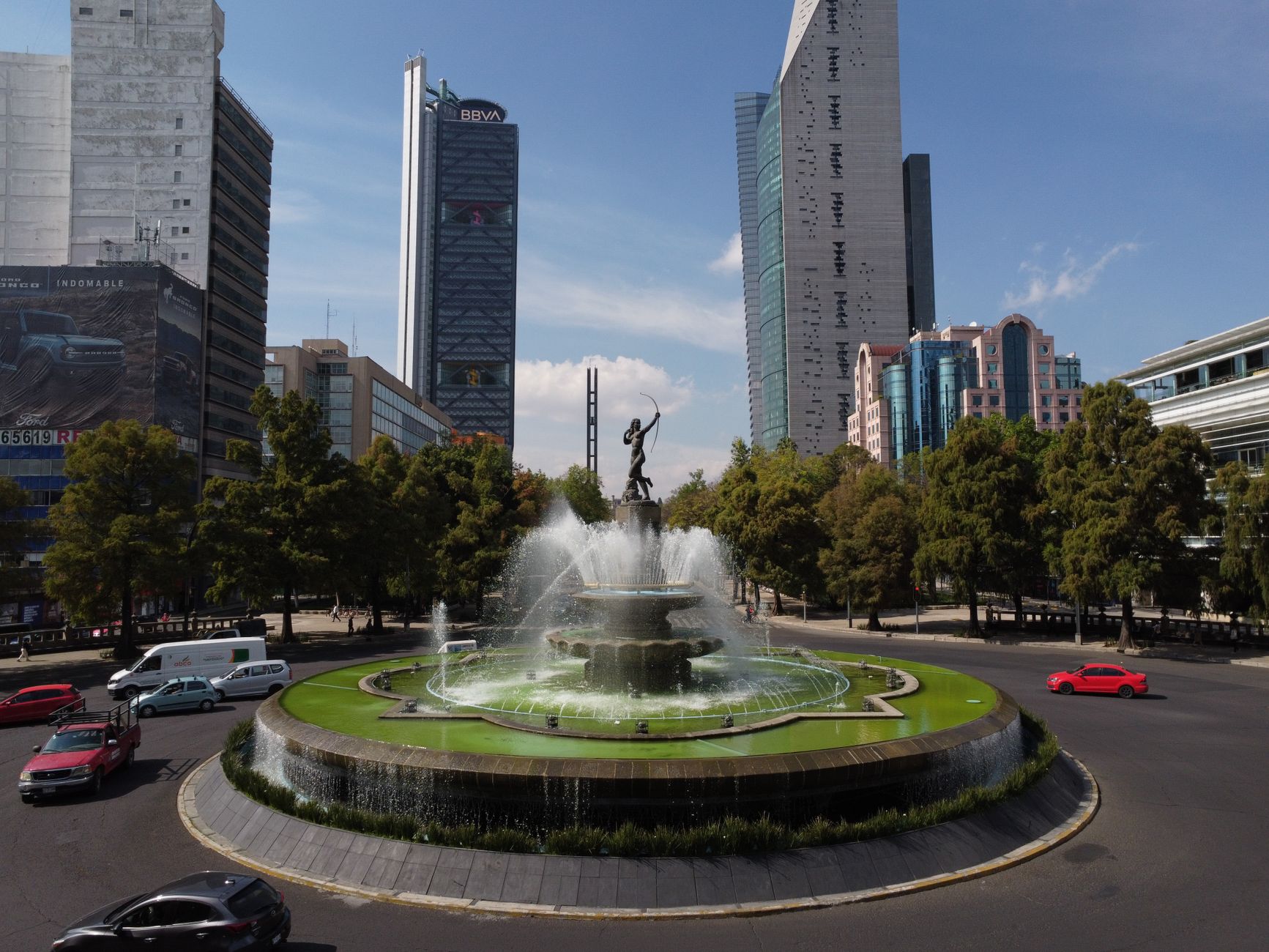Scenic view of a roundabout featuring a central fountain surrounded by skyscrapers on a sunny day.