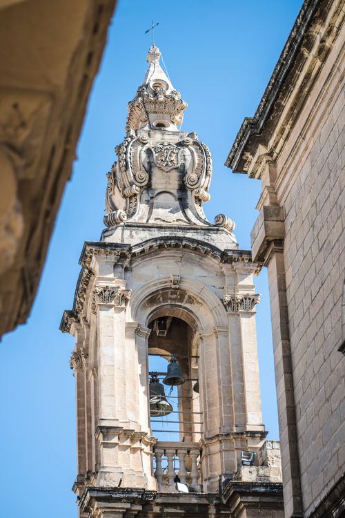 Free A detailed view of a historic Baroque bell tower with intricate carvings and a clear blue sky backdrop. Stock Photo