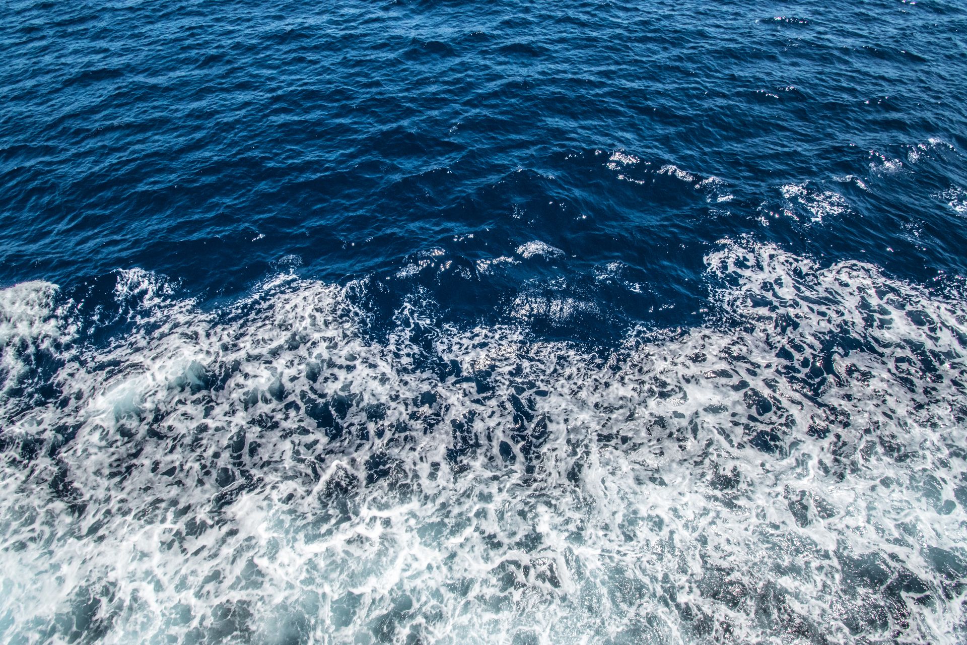 Aerial view of the ocean's dynamic waves and seafoam, showcasing its vibrant blue hues.