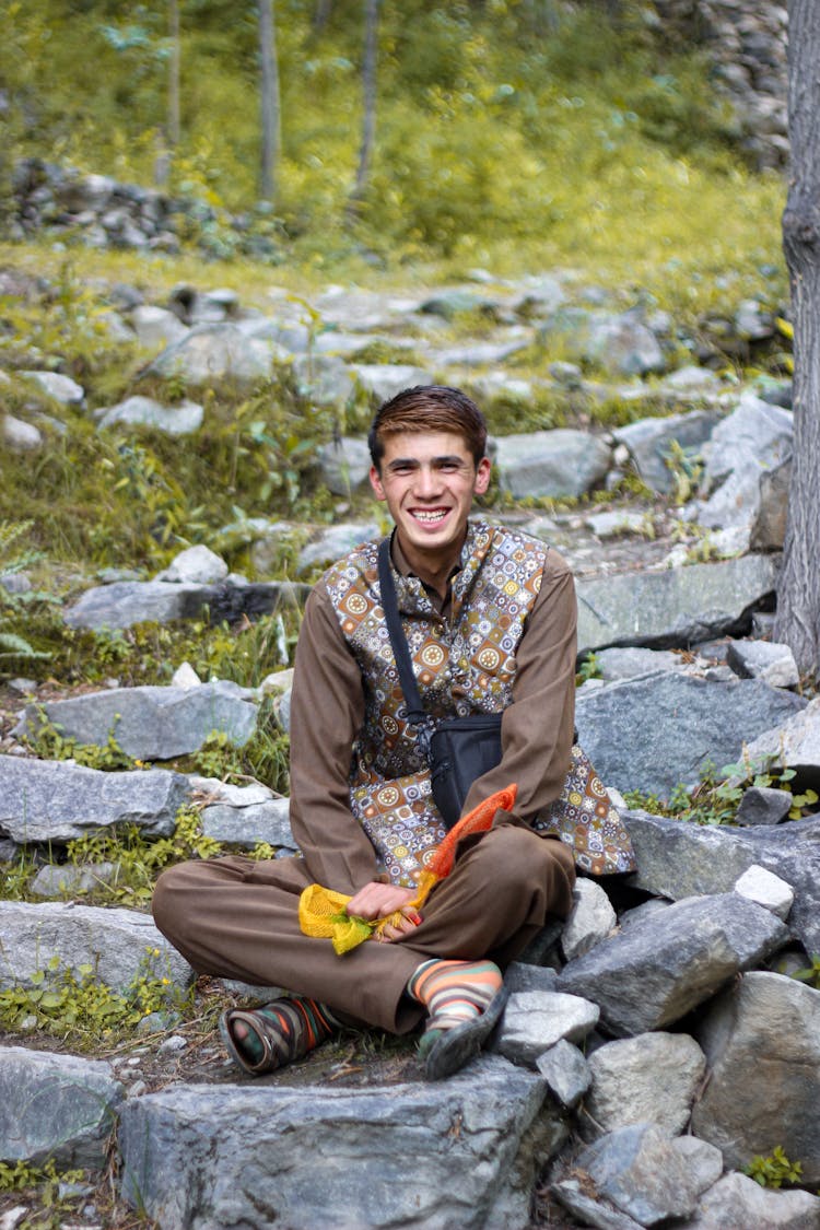 Man With A Black Sling Bag Sitting On Gray Rocks