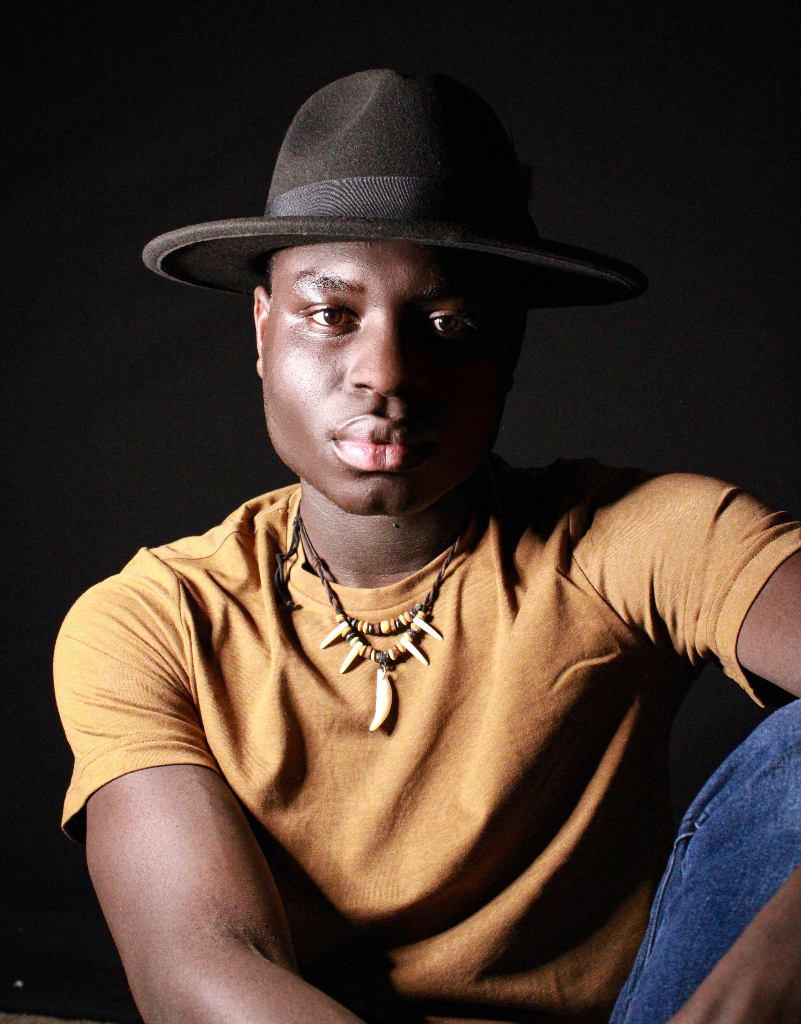 Close-up portrait of a serious man in a yellow shirt and fedora hat.