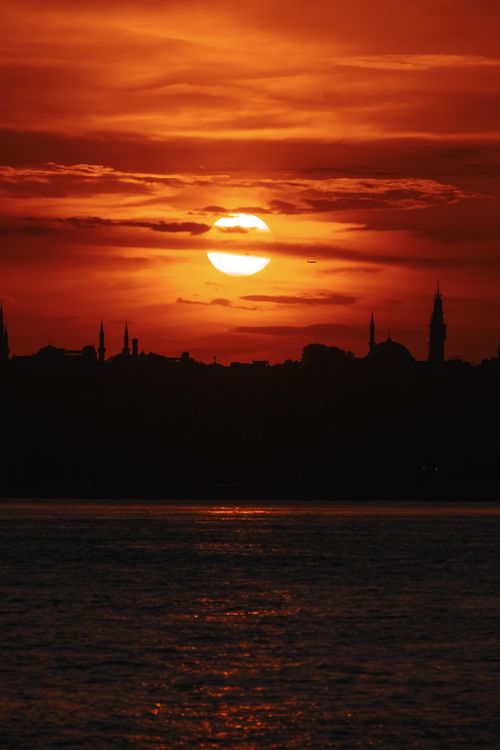 Free A stunning sunset casts a golden glow over a silhouetted city skyline with an orange sky. Stock Photo