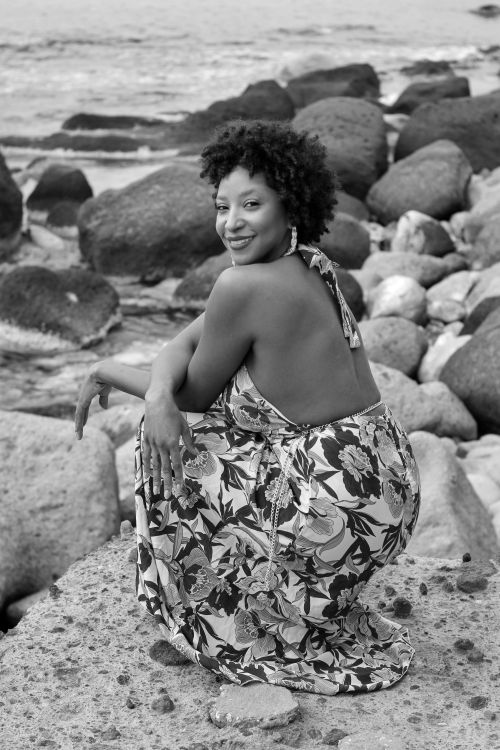 Free Smiling woman in floral dress sits on rocks by the ocean in black and white. Stock Photo