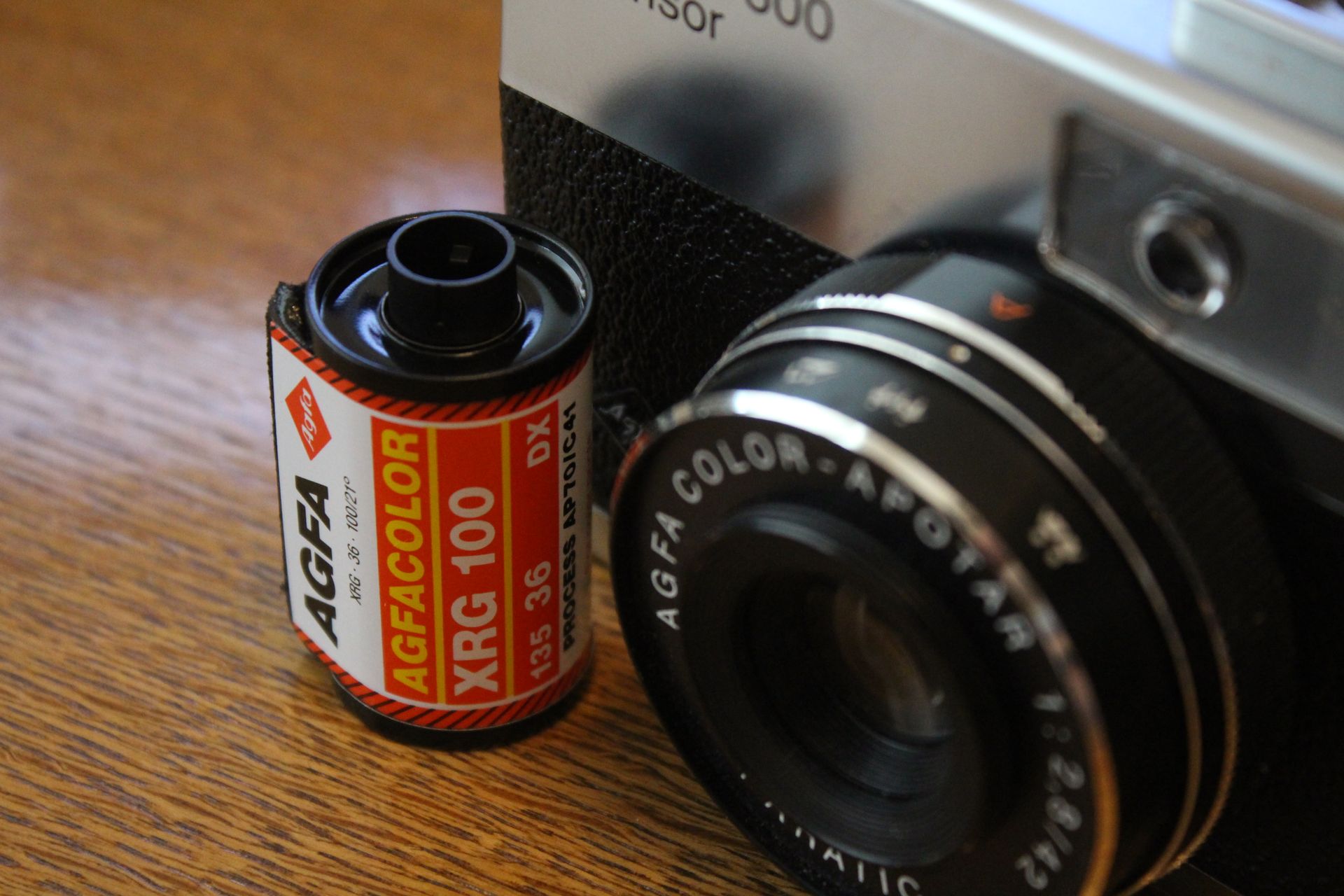 Vintage camera detail with Agfa Agfacolor XRG 100 film roll on wooden surface.