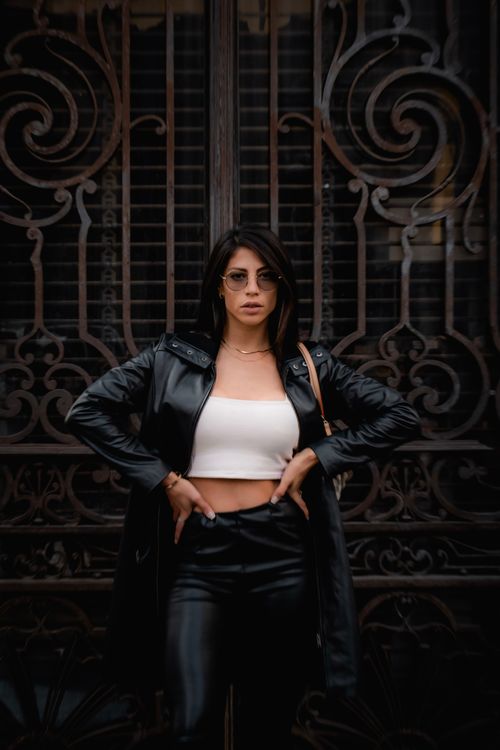 Free Confident woman in chic leather attire stands poised against an ornate metal gate, showcasing urban fashion. Stock Photo