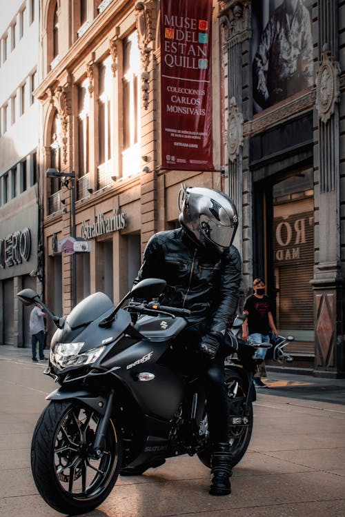 A Person in Black Leather Jacket Wearing Gray Helmet while Riding a Motorcycle