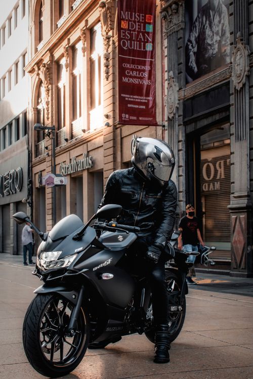 Free A motorcyclist in black leather gear and helmet rides through a bustling city street. Stock Photo