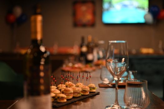 Close-up of a classy table setup with mini burgers, wine glasses, and elegant decor.
