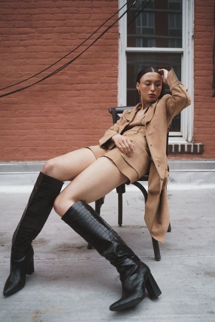 Fashionable woman in a tan coat and boots sitting outdoors in New York City.