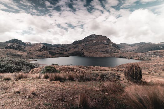 A breathtaking view of a serene lake surrounded by rugged mountains under a cloudy sky.