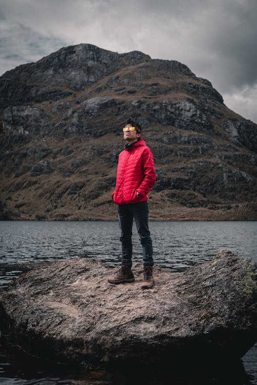 A Man in Red Jacket Standing on Big Rock Near the Lake 