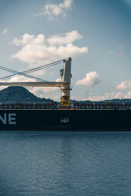 Free A cargo ship docked at a harbor under a clear blue sky with mountainous background. Stock Photo