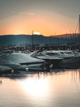 A tranquil evening view of yachts docked by the Geneva marina during sunset, reflecting on calm waters.