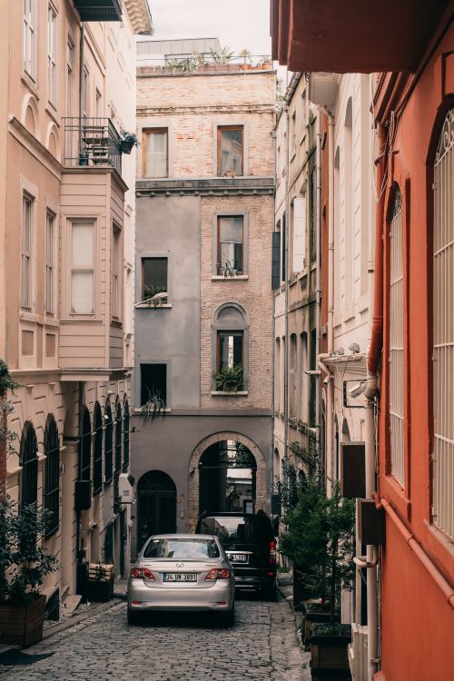 Free Narrow cobblestone street with parked cars and colorful buildings, perfect for travel inspiration. Stock Photo
