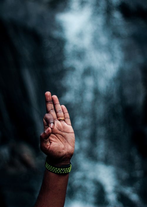 Free A close-up of a hand gesture in front of a blurred waterfall in Wayanad, India. Stock Photo