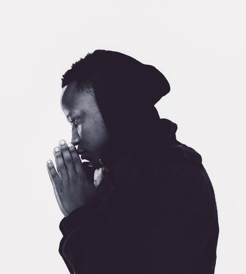 Free Side profile of a man in a hoodie praying, captured in a striking black and white tone. Stock Photo