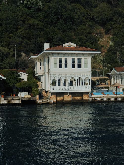 Free Elegant white villa perched over tranquil riverside, framed by lush greenery. Stock Photo