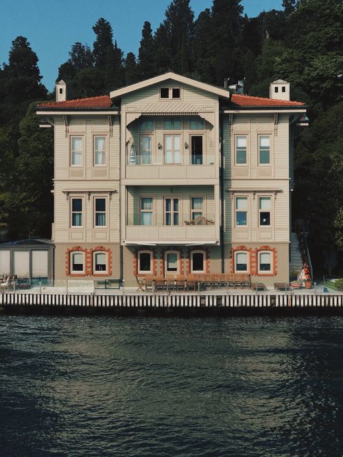 Free Beautiful mansion by the lake with serene water and lush forest backdrop. Stock Photo