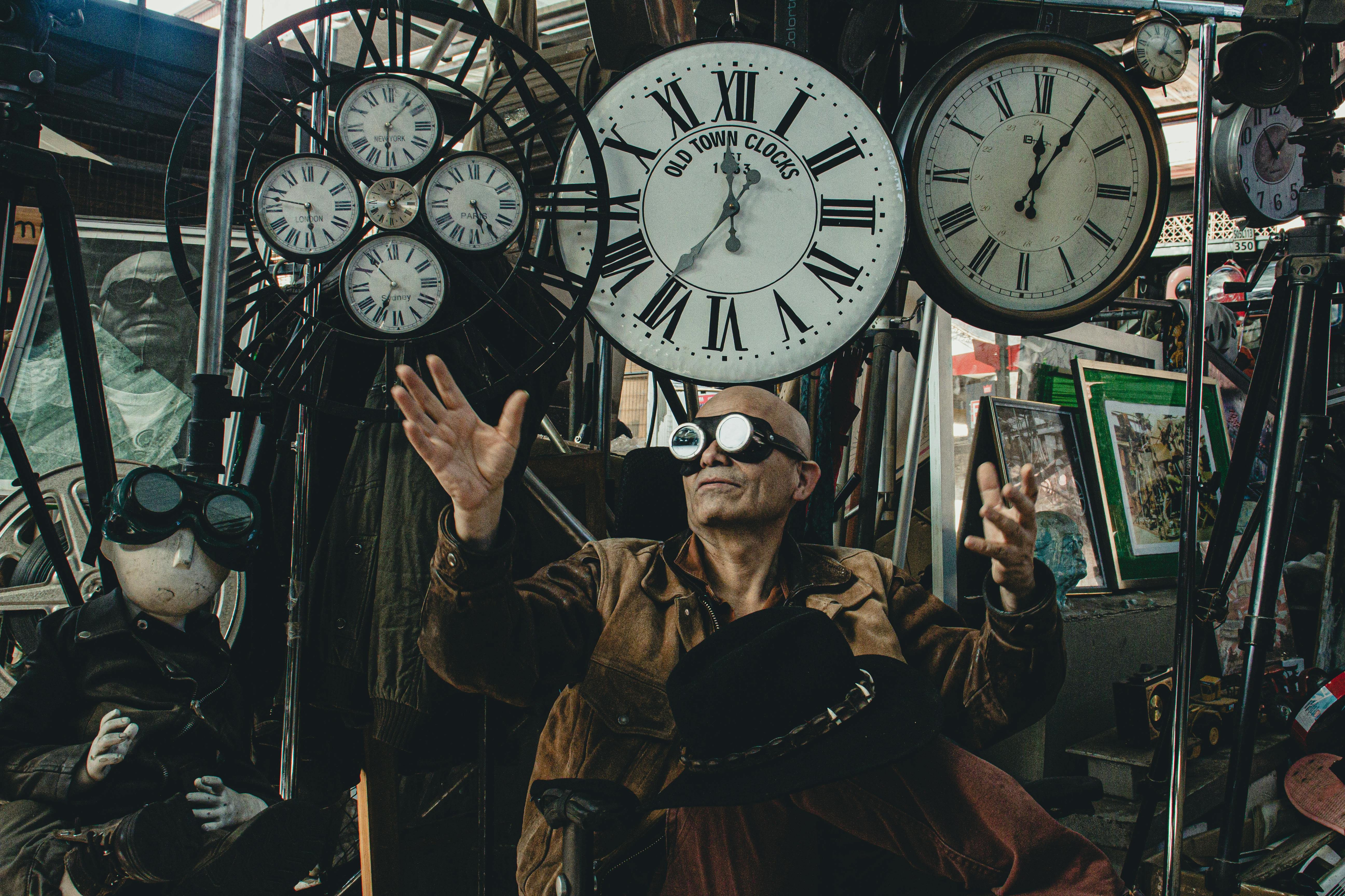 Man in Brown Leather Jacket Standing Beside Vintage Analog Wall Clocks