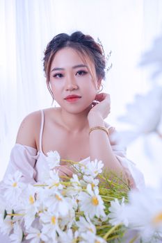 Close-up portrait of a woman holding white daisies, exuding elegance and serenity.