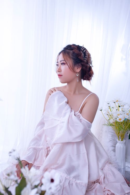 Free A beautiful bride in elegant attire sits gracefully by a window adorned with flowers. Stock Photo