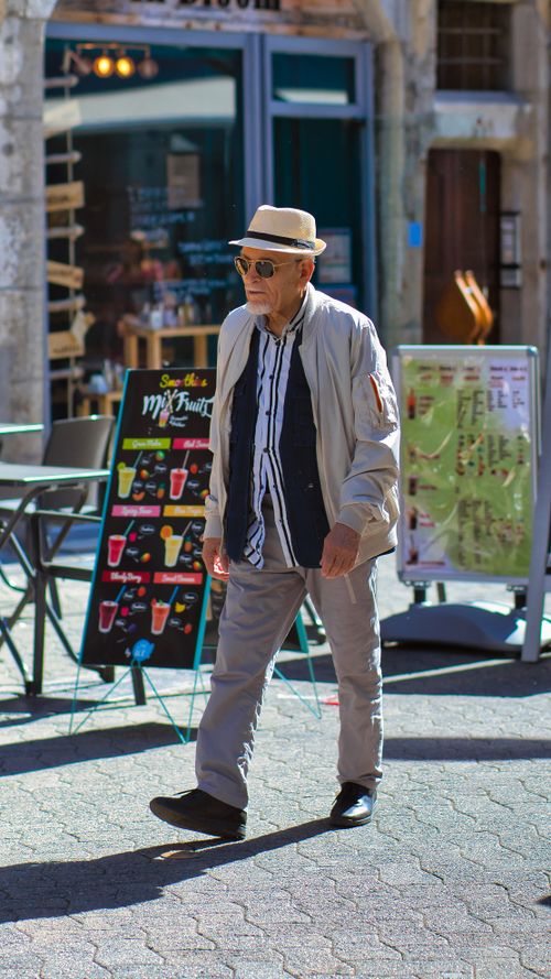 Free Senior man in casual attire and sunglasses walking in a lively urban setting. Stock Photo
