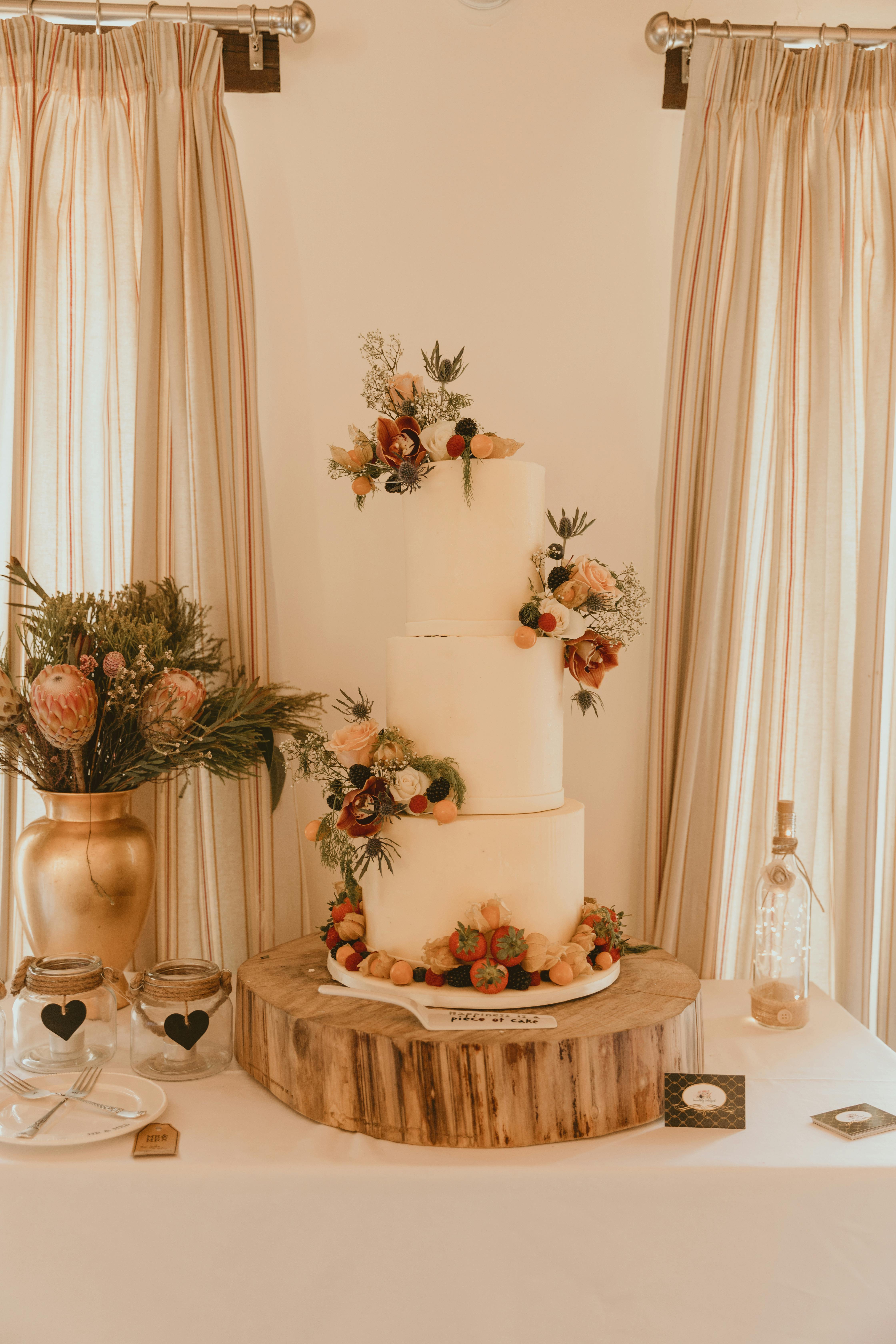 A beautifully decorated wedding cake with floral accents on a rustic wooden stand indoors.