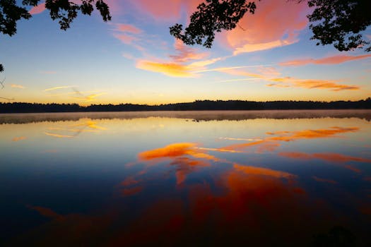 A serene lake reflecting a vibrant sunrise with calm water and colorful clouds.