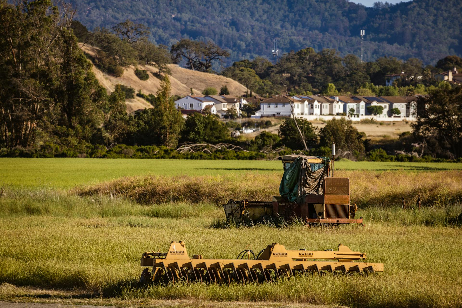 Scenic rural landscape featuring farming equipment and countryside homes against a green field backdrop.