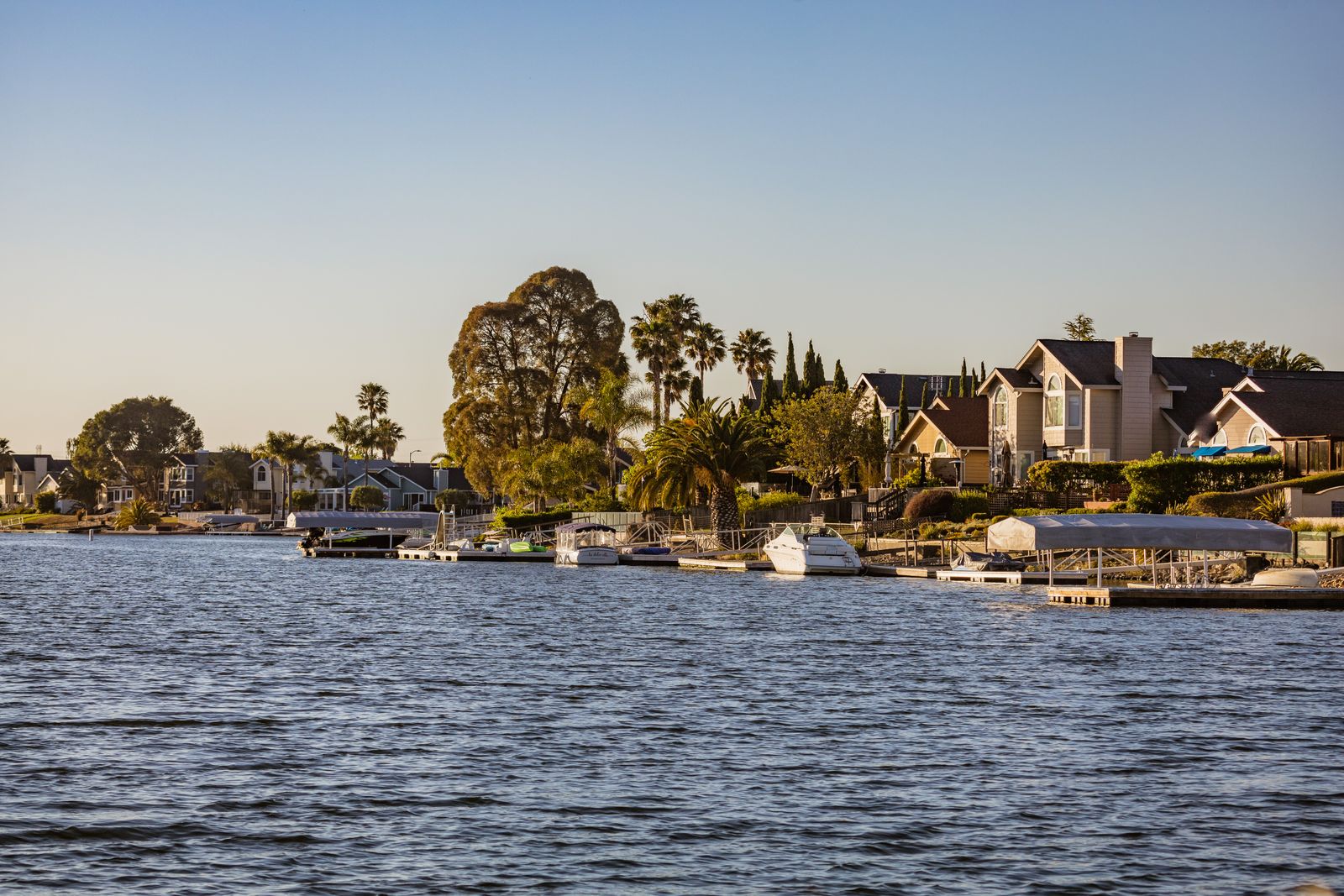 A calm shoreline lined with waterfront homes and docks under clear midday light.