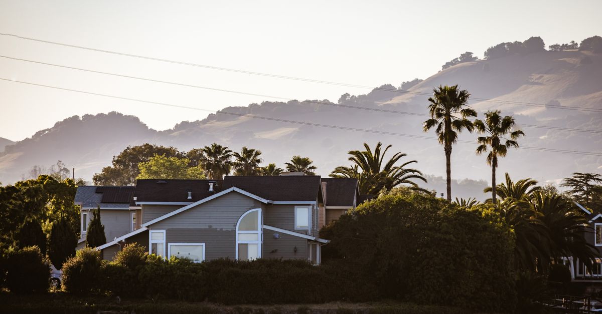 Beautiful lakeside house surrounded by palm trees and hills, offering a serene landscape view.